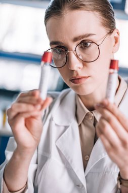 Gözlüklü güzel immünolojistin test tüplerine baktığı seçici odak. 