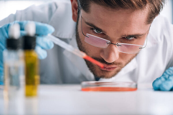 selective focus of immunologist holding pipette with red liquid 