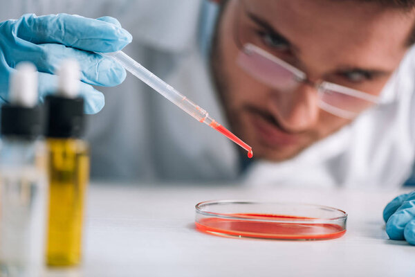 selective focus of immunologist holding pipette with red liquid in lab 
