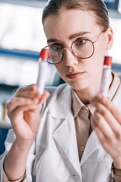 selective focus of beautiful immunologist in glasses looking at test tubes 