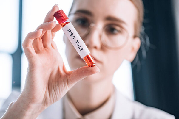 selective focus of attractive immunologist in glasses looking at test tube with psa test letters 