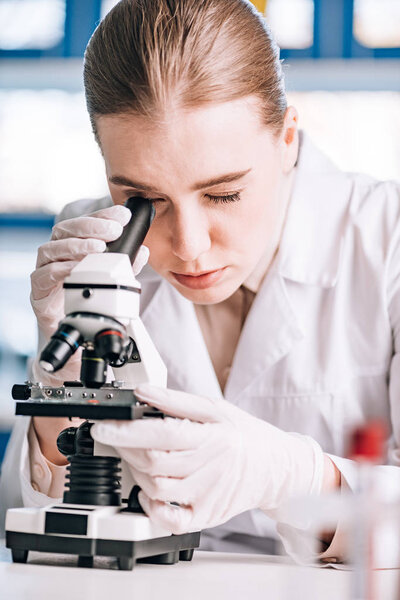 selective focus of immunologist in latex gloves looking through microscope 