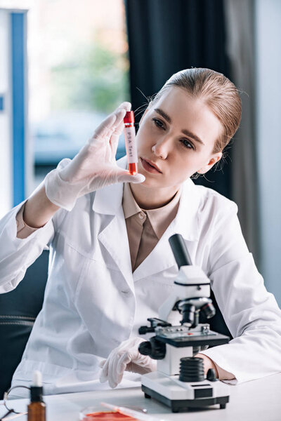selective focus of attractive immunologist in latex gloves looking at test tube near microscope 