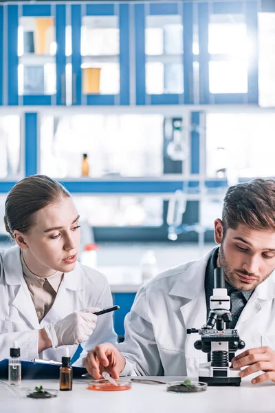 Attraktiver Biochemiker Schaut Mitarbeiter Der Nähe Des Mikroskops — Stockfoto