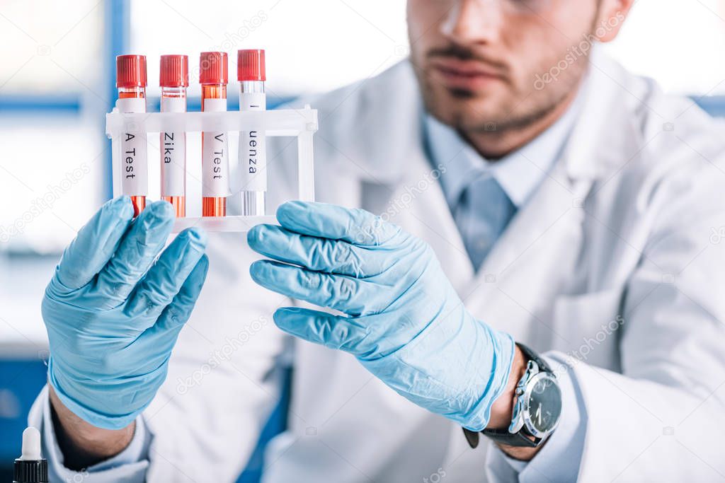 cropped view of bearded immunologist holding test tubes with letters 