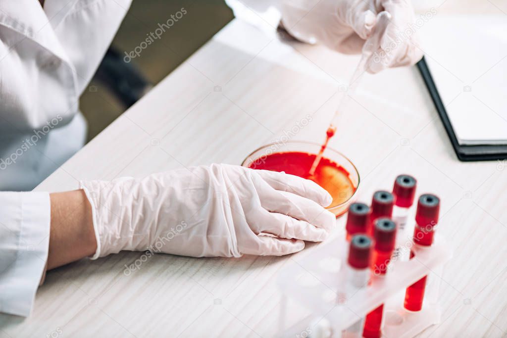 cropped view of immunologist holding pipette with red liquid in laboratory 