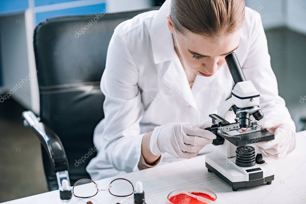 immunologist looking through microscope near glasses on table