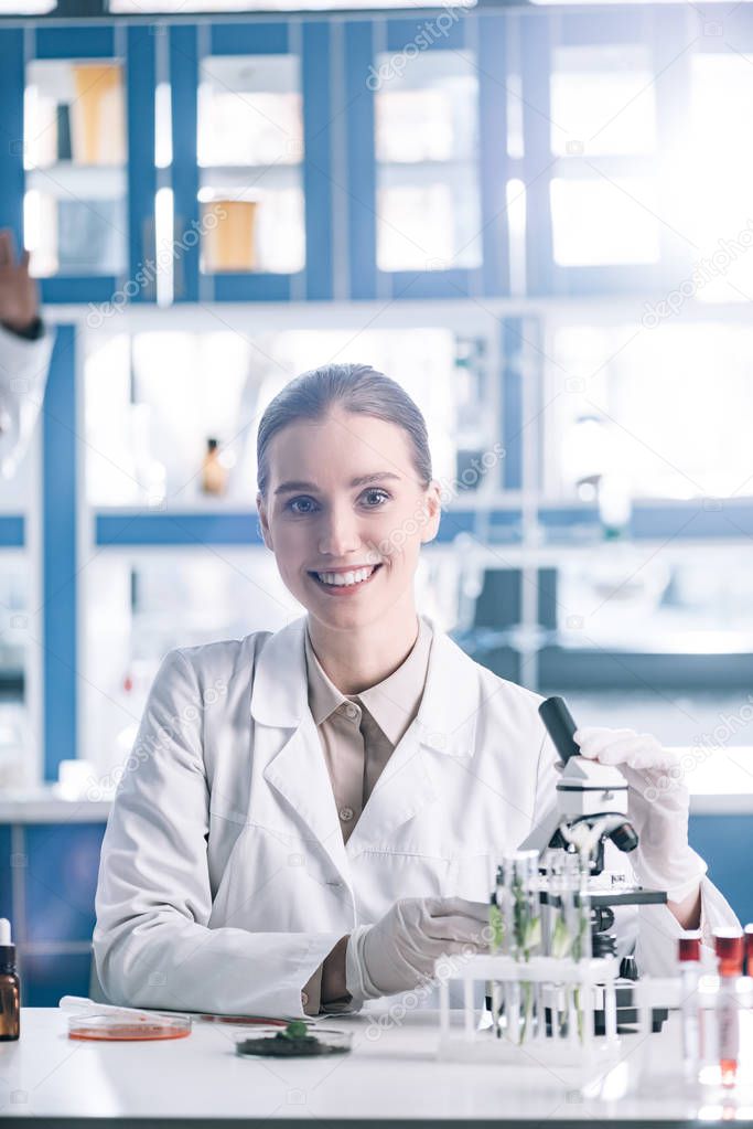 selective focus of happy scientist in white coat near microscope 