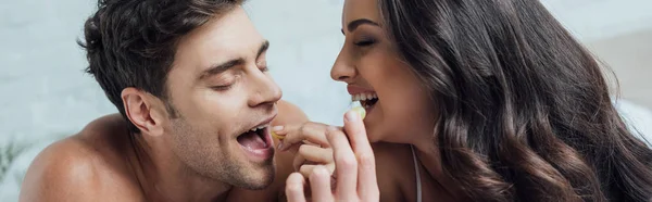 panoramic shot of cheerful couple feeding each other with grapes