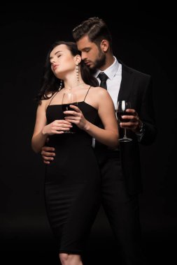 Yakışıklı bir adam ve güzel bir kadın ellerinde kırmızı şarapla siyah bardaklar. 