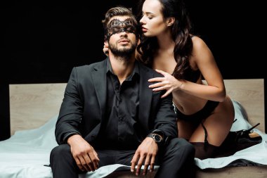 seksi kadın iç çamaşırlı, gözleri bağlı, siyah bir adamın yanında oturuyor. 