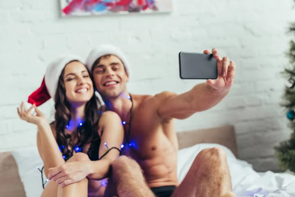 Veselý Pár Spodním Prádle Santa Klobouky Přičemž Selfie Smartphone Posteli — Stock fotografie