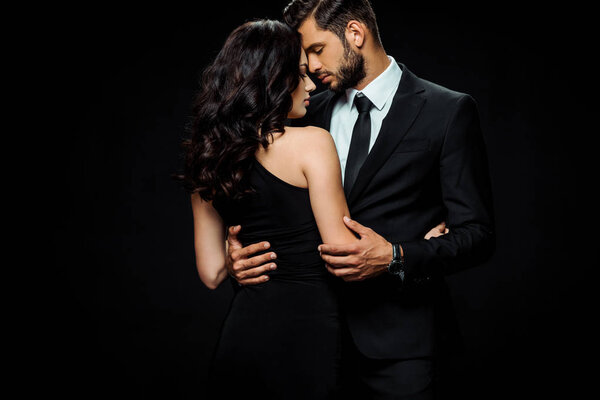 attractive woman in dress hugging bearded man isolated on black 
