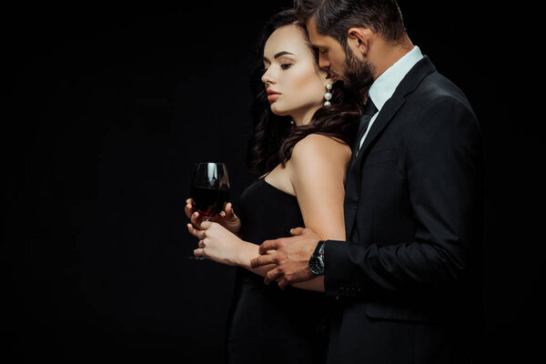 бородатый мужчина касается привлекательной женщины с бокалом красного вина изолированы на черном
 
