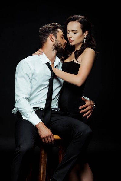 attractive woman touching bearded boyfriend in shirt sitting on chair isolated on black 