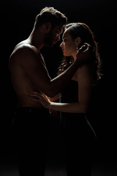 side view of shirtless man touching attractive woman isolated on black 