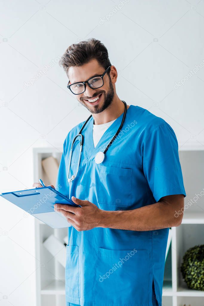 handsome veterinarian smiling at camera while writing prescription on clipboard