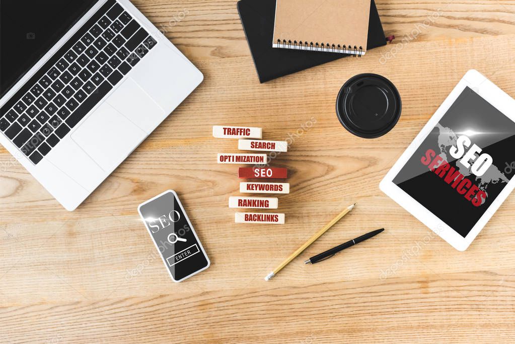 top view of wooden rectangles with illustration of concept words of seo, digital devices, notebooks, pen, paper cup and pencil 