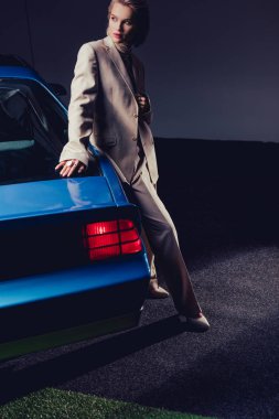 Çekici ve şık takım elbiseli kadın retro arabanın yanında duruyor. 