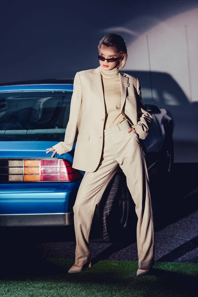 レトロな車の近くに立つスーツやサングラスを着た魅力的でスタイリッシュな女性 — ストック写真