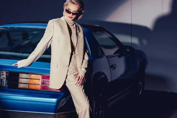 レトロな車の近くに立つスーツやサングラスを着た魅力的でスタイリッシュな女性 — ストック写真