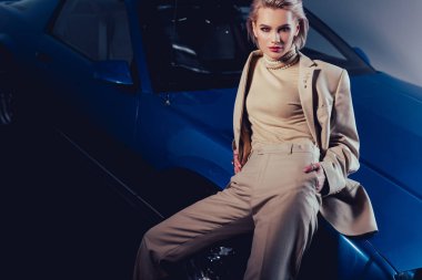 Çekici ve şık takım elbiseli kadın eski arabanın üzerinde oturuyor. 