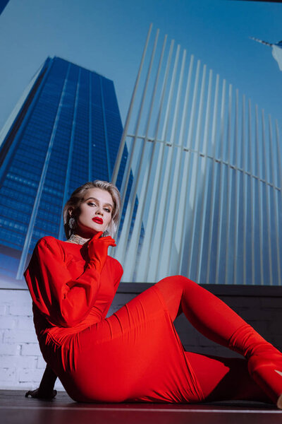 attractive and stylish woman in red dress sitting on city background 