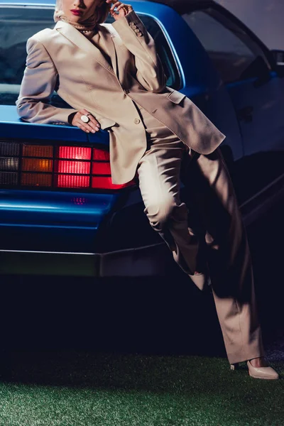 cropped view of stylish woman in suit lying on retro car