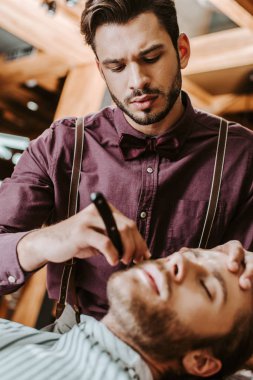 selective focus of handsome and stylish barber shaving man  clipart