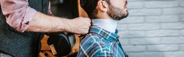 panoramic shot of barber fixing collar around neck of bearded man  clipart