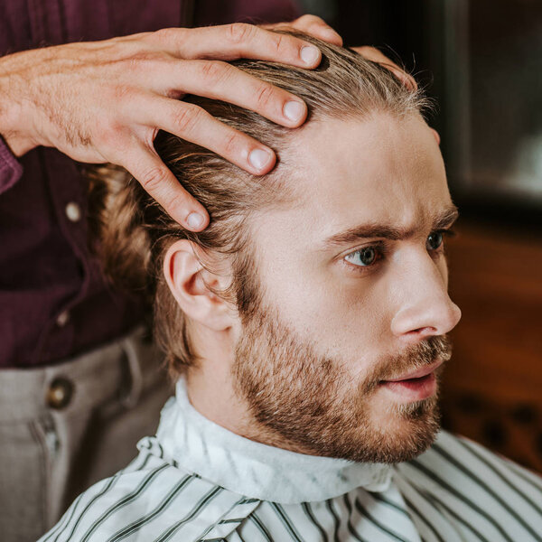 close up of barber putting hands on hear of handsome bearded man 