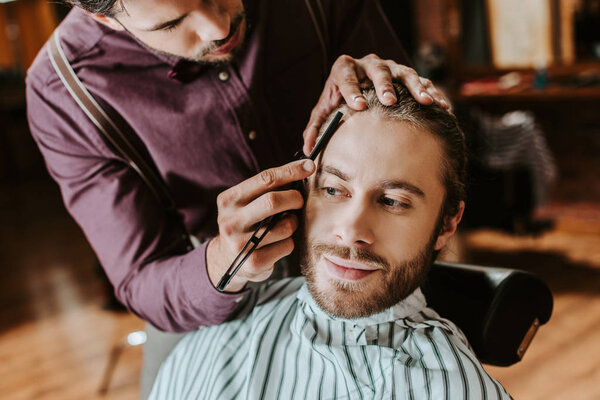 barber shaving happy bearded man in barbershop 