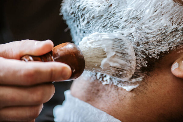 close up of barber applying shaving cream on face of man 
