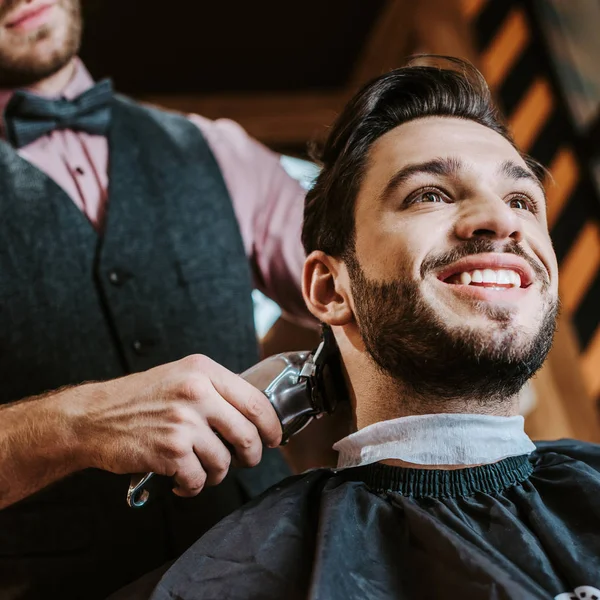 理髪店で幸せな男の髪をスタイリングしながら 床屋保持トリマーの低角度ビュー — ストック写真