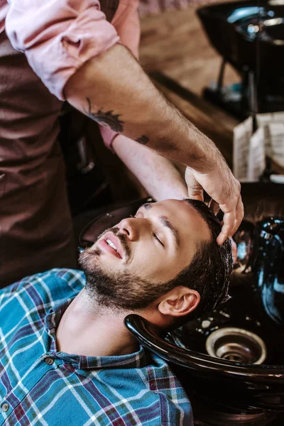 Tätowierter Friseur Wäscht Haare Eines Gutaussehenden Mannes Mit Geschlossenen Augen — Stockfoto