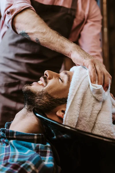 Peluquero Tatuado Sosteniendo Toalla Blanca Cerca Cabeza Del Hombre Feliz — Foto de Stock