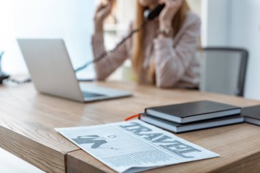 selective focus of travel newspaper and notebooks on desk near travel agent talking on phone clipart