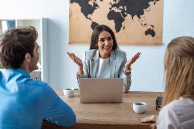 smiling travel agent gesturing while talking to couple of tourists clipart