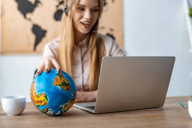 Gülümseyen seyahat acentesinin laptopa bakarken dünyaya dokunuşunun seçici odağı