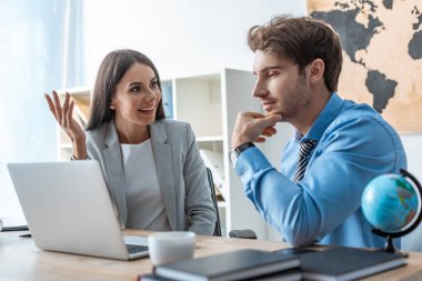 smiling travel agent talking to thoughtful man looking at laptop screen clipart