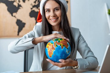 happy travel agent holding globe and smiling at camera clipart