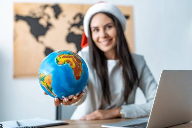 cheerful travel agent showing globe and smiling at camera clipart