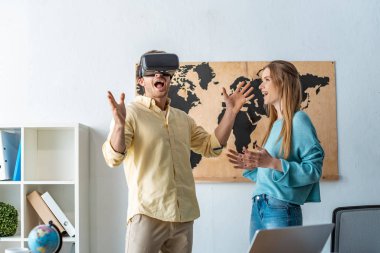 Gülümseyen seyahat acentesi VR kulaklık kullanarak heyecanlı müşteriye bakıyor