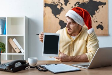 Noel Baba şapkalı sürpriz seyahat acentesi elinde boş ekranlı dijital tablet tutuyor.