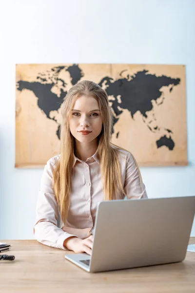 Attraktives Reisebüro Blickt Die Kamera Während Neben Dem Laptop Sitzt — Stockfoto