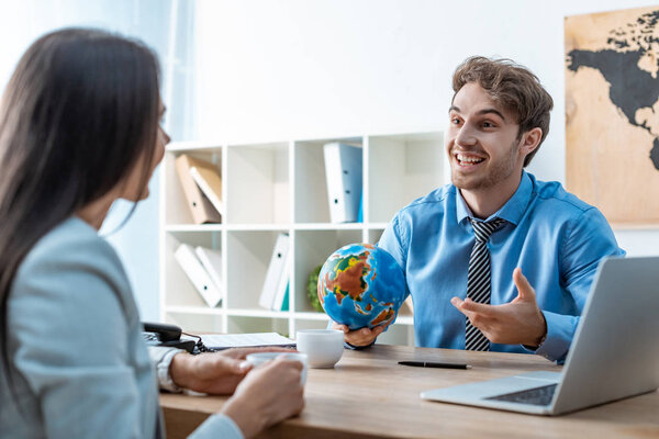 cheerful travel agent holding globe while talking to client