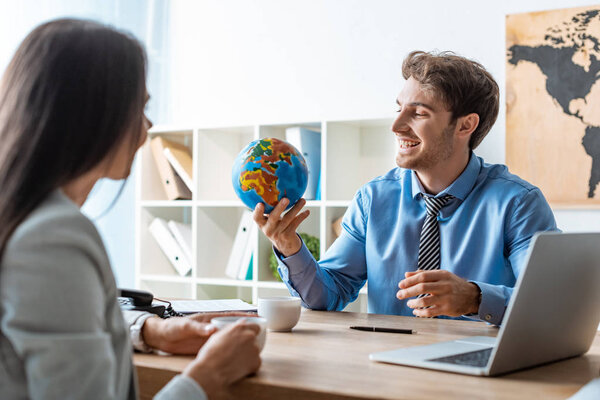 cheerful travel agent holding globe while talking to client