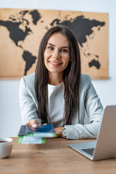selective focus of smiling travel agent holding passports and air tickets