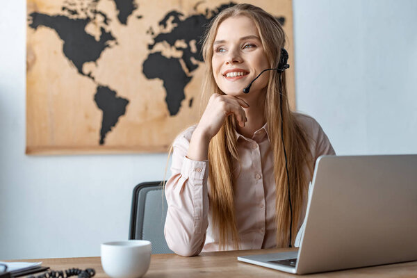 smiling travel agent looking away while sitting at workplace