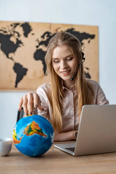 Smiling Travel Agent Touching Globe While Sitting Workplace — ストック写真